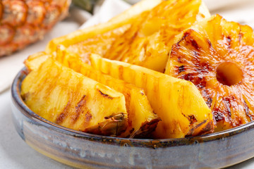 Heap of grilled pineapple slices on gray plate on concrete background.