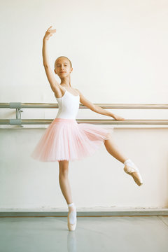 Cute little ballerina in pink ballet costume and pointe shoes is dancing near ballet barre. Kid in dance class. Child girl is studying ballet. Copy space.