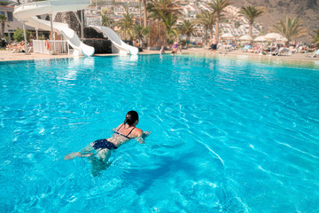 slender woman swims in the pool in a resort hotel