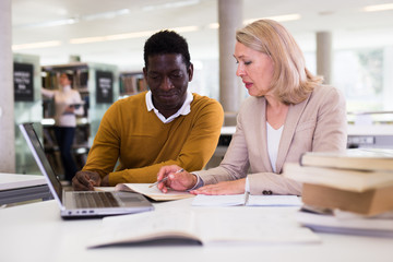Obraz premium Female teacher working with african-american man in university library