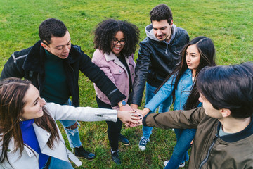 Group of young friends at the park join hands in the center of a circle to give unity and strength...