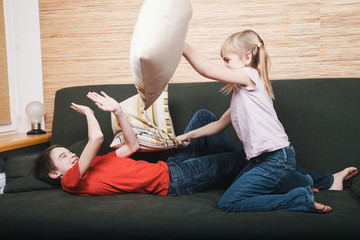 Siblings losing they mind confined at home during self-isolation having pillow fight on a couch