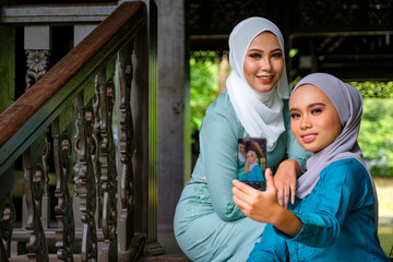 Muslim Malay women wearing hijab and traditional costume are taking selfie during Aidilfitri celebrations at the terrace of traditional wooden house.