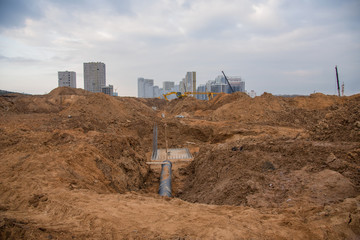 Excavator at construction site during laying sewer and main reticulation systems. Civil infrastructure pipe, water lines, sanitary sewers and storm sewers. Underground utilities installation