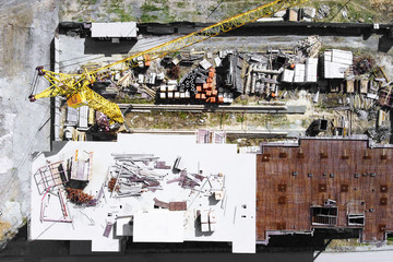 Fototapeta premium Building object surrounded by metal fence, top view from height. Yellow crane, building materials and unfinished high-rise building at construction site. Utility room trailer for workers and watchman.