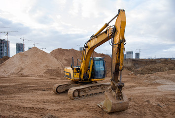 Obraz premium Yellow excavator during earthworks at construction site. Backhoe digging the ground for the foundation and for laying sewer pipes district heating. Earth-moving heavy equipment