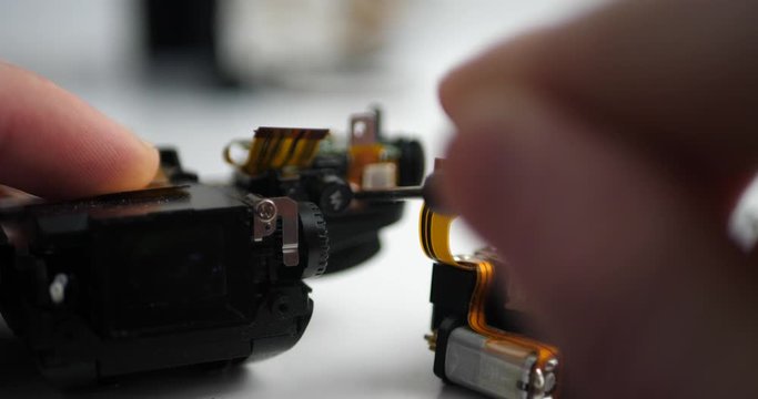 Closeup of electrical engineer disassembling camera parts on the desk in workshop. Broken camera for service repairs. Unscrewing components.