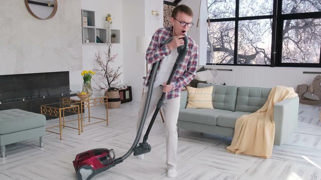 Cheerful man doing the cleaning and dancing with a vacuum cleaner, slow motion
