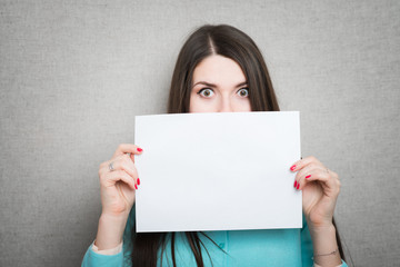 Banner sign woman peeking over edge of blank empty paper billboard with copy space for text. Beautiful Asian Caucasian woman looking surprised and scared - funny. Isolated on white background.