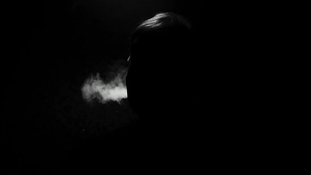 the silhouette of a man on a dark background exhales clouds of smoke