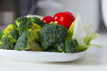 Healthy lifestyle concept: Vegetables (cabbage, tomato, broccoli) on a white plate on a white table