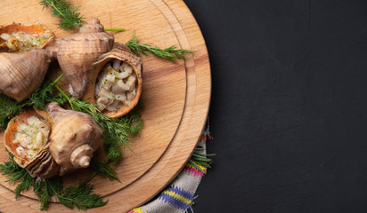 cooked rapa whelk with dill on a wooden round board with, dark background