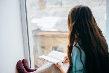 Young girl reading with book by the window