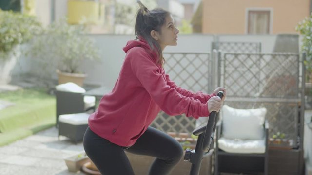 Cheerful girl pedaling on exercise bike on terrace