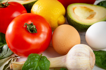 fresh avocado,  tomatoes, red sweet pepper, lemon, spinach, eggs, onion, garlic on a white ,   healthy food, close up