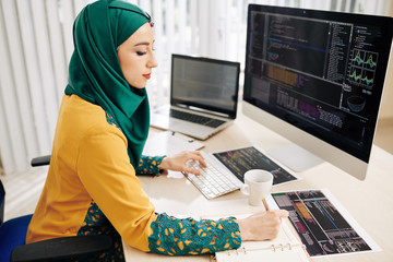 Young muslim female software developer working on programming code and taking notes in planner