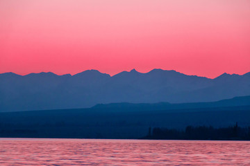 Beautiful pink sunset with mountain silhouettes and pink reflection of the lake