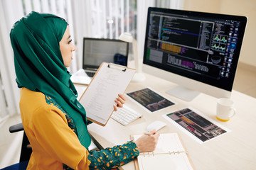 Serious pensive young muslim software developer looking on programming code on computer screen and...