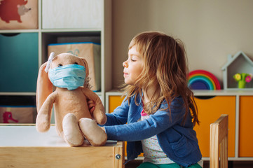Toddler girl playing with rabbit soft toy in the medicine mask