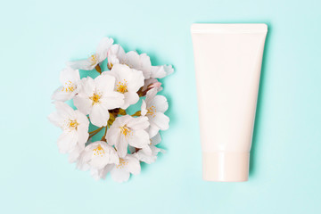 White tube of cream and sakura flowers on blue background top view.