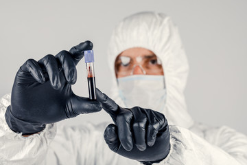 A test tube in a man's hand close-up , a man in a medical mask holding a bottle of red liquid....