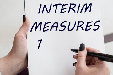 words INTERIM MEASURES writes girl on a blank white sheet