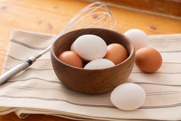 Raw eggs in a wooden bowl and on a clean cloth with a blender aside in warm light and wooden background