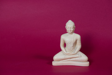 white statue of a Thai Buddha in sitting meditation on a red background