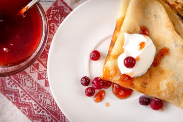 pancakes with sour cream, berries, cranberries and jam on a plate, tea, jam on a towel with a red pattern on a white