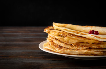 Russian pancakes with berries on a plate on a dark wooden background, side view