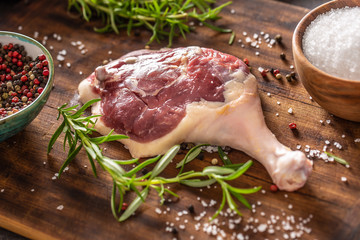 Close-up view of a duck leg with skin on, black, red and white pepper, fresh rosemary and salt in a...