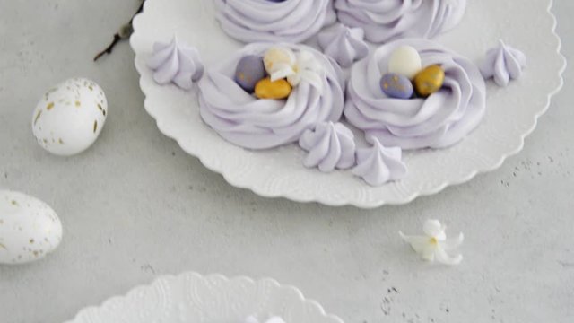 Easter bird nest meringue cookies - lilac mini Pavlova desserts with pastel candy eggs in nest shape for Easter holiday party. Side view, close up. Confectionery, bakery concept