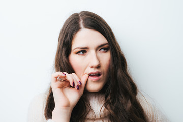 brunette girl bites his nails on a white background