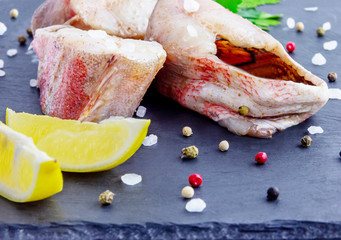 Red grouper steak with lemon, basil on a dark boards