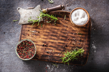 Top of view shot of square wooden cutting board and rustic cleaver on dark background with spices,...