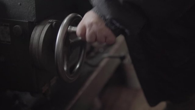 Old worker quickly rotates the crank of a metal lathe machine