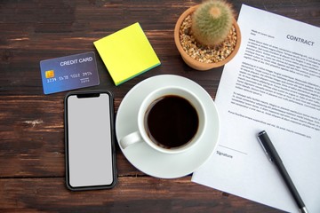 A desk preparation for signing a contract, comprising of contract, coffee, mobile phone, credit card