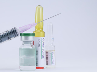 Close shot of an injection needle with generic ampoules and Coronavirus vaccine labels.
