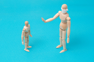 Concept - take care of the health of loved ones, keep your distance during quarantine. One wooden man mannequin in protective medical mask holds hands in front of him refusing contact with small child