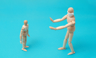 Concept - take care of the health of loved ones, keep your distance during quarantine. One wooden man mannequin in protective medical mask holds hands in front of him refusing contact with small child