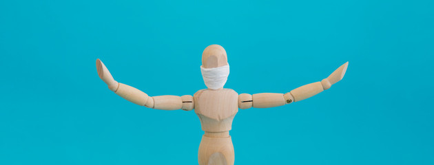 Concept - keep your distance during quarantine. Wooden man mannequin in a protective medical mask holds his hands in different directions standing on a blue background.