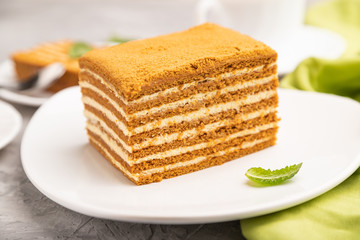 Homemade honey cake with milk cream and mint with cup of coffee on a gray concrete background. Side view, selective focus.