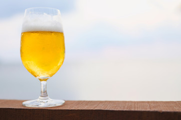 Mug of cold beer with foam on the table. Against the background of the sea in Restaurant