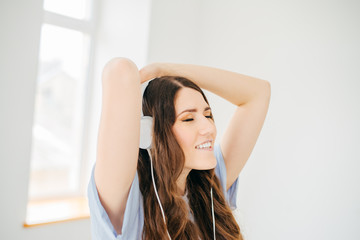 Fototapeta premium Happy girl dancing at home while listen music with headphones. She is in her house in front of the big window in nature view