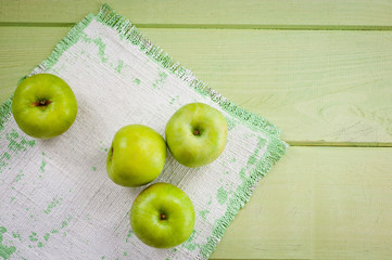 Ripe green apples on a green napkin lying on a canvas napkin and a wooden table surface. Background for fruits.