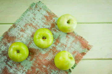 Ripe green apples on a green napkin lying on a canvas napkin and a wooden table surface. Background for fruits.
