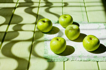 Ripe green apples on a light green painted wooden surface, illuminated by sunlight from a window through curtains. Background for fruits. Black and white drawing with natural light.