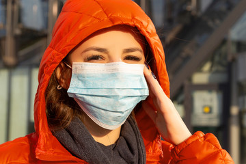 A woman wears a protective mask against allergies, viruses, air pollution. Climate change concept. Portrait of a young woman in a medical mask from a coronavirus in a red jacket on the street.