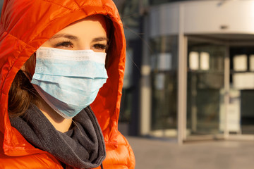 A woman wears a protective mask against allergies, viruses, air pollution. Climate change concept. Portrait of a young woman in a medical mask from a coronavirus in a red jacket on the street.