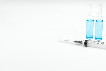 A syringe and two glass ampoules with the drug in blue on a white background and a place for the inscription. The vaccine is used for prevention, immunization and treatment of coronavirus infection.